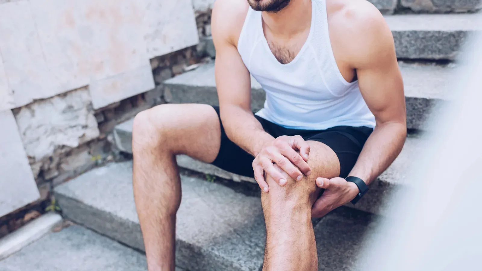 A man in sportswear sitting on concrete steps, both hands around his knee