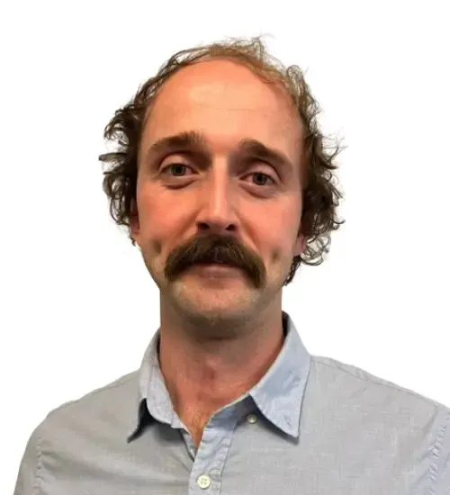Head and shoulders portrait of a physiotherapist with curly hair and a moustache, in a light blue shirt