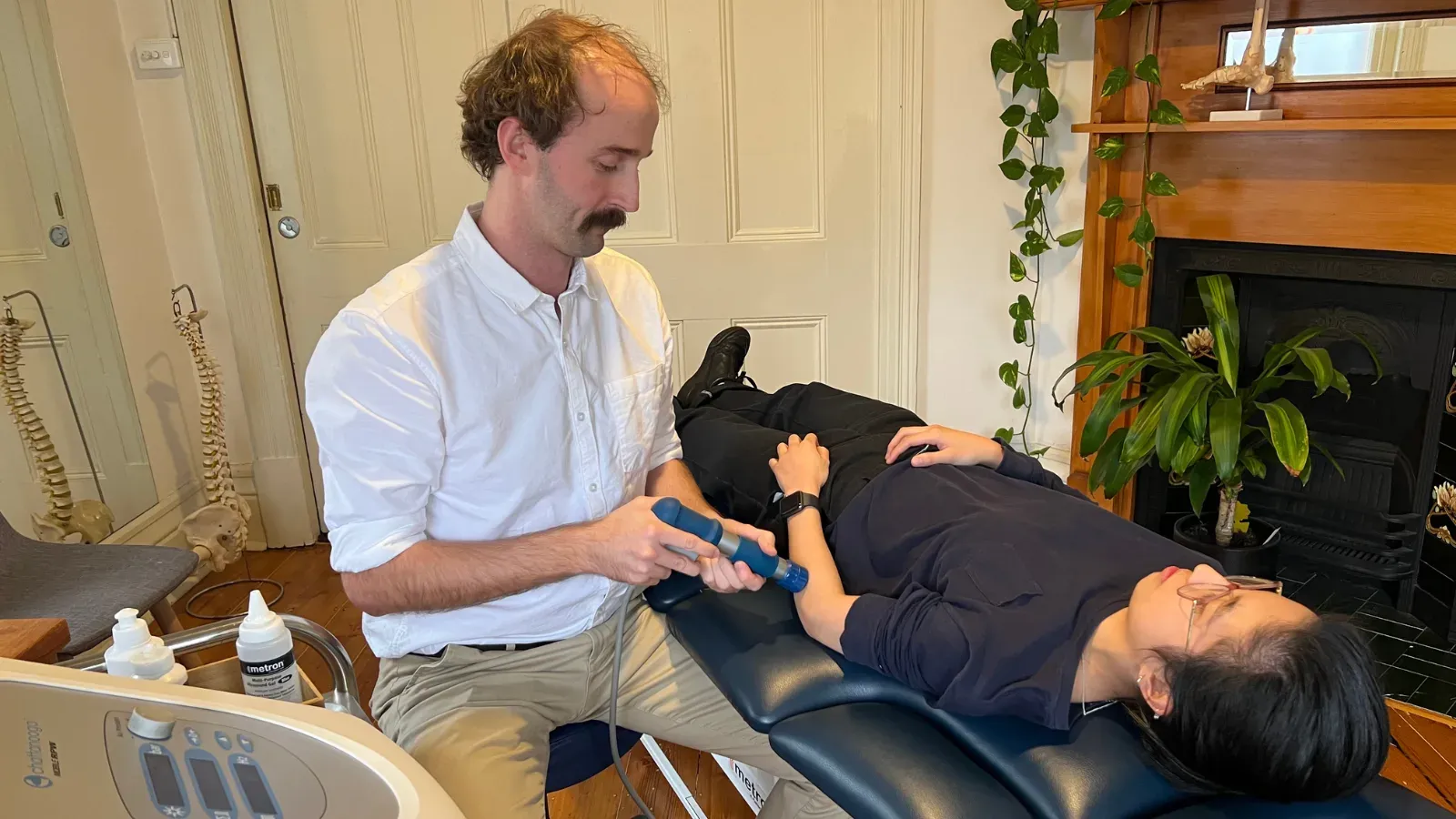 A physiotherapist applying a shockwave handpiece to a patient's leg in the clinic