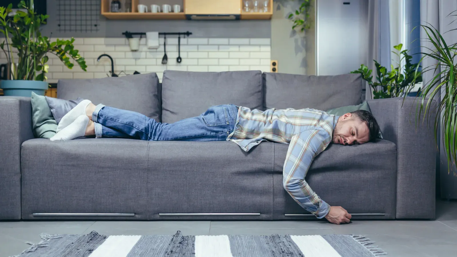A person lying face down and fully clothed across a sofa in the middle of the day