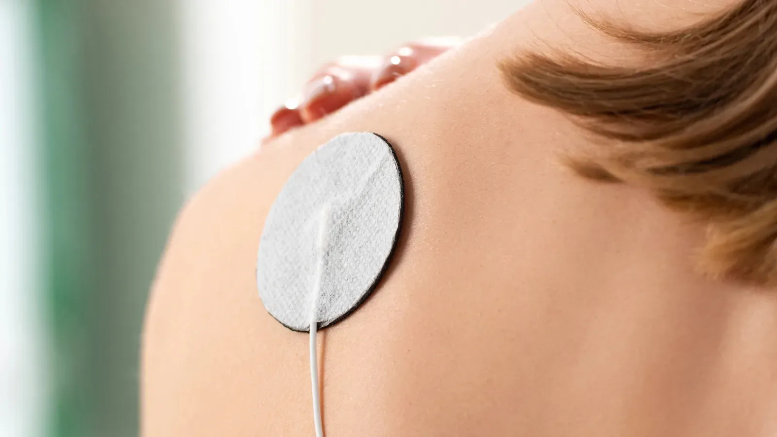 A single TENS electrode pad placed on a person's shoulder, its lead trailing away