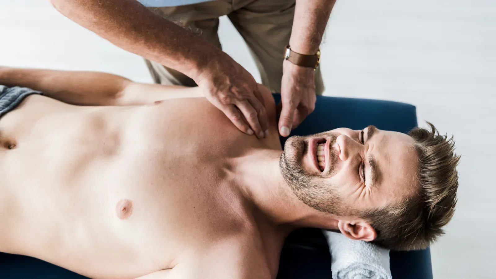 A physiotherapist working on the front of the shoulder of a patient lying on a treatment table