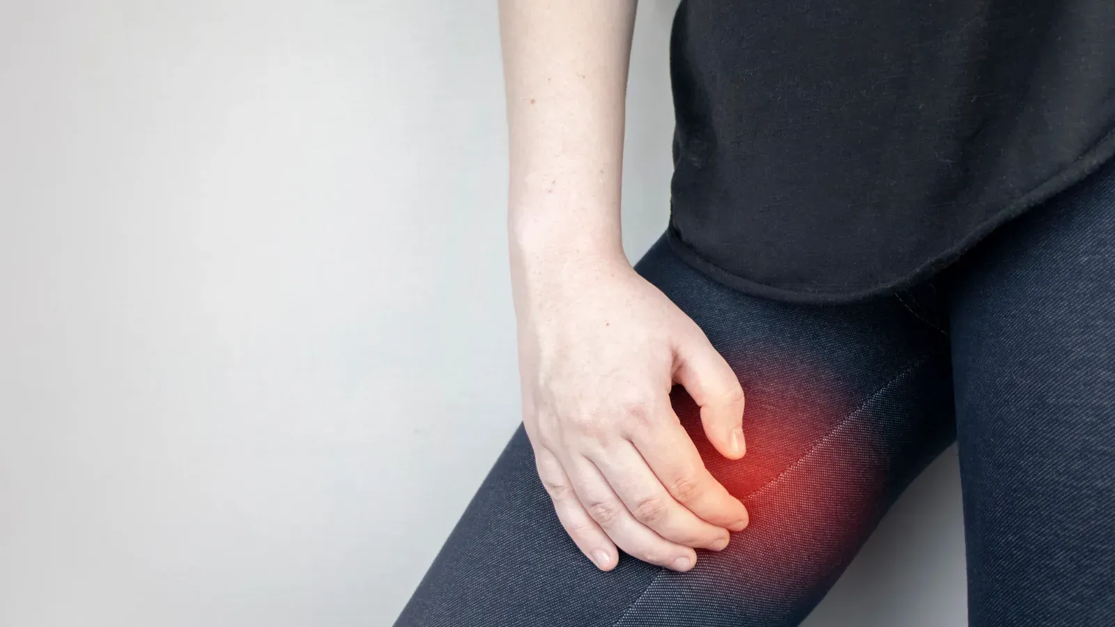 A person in leggings pressing a hand to their upper inner thigh, the area highlighted in red