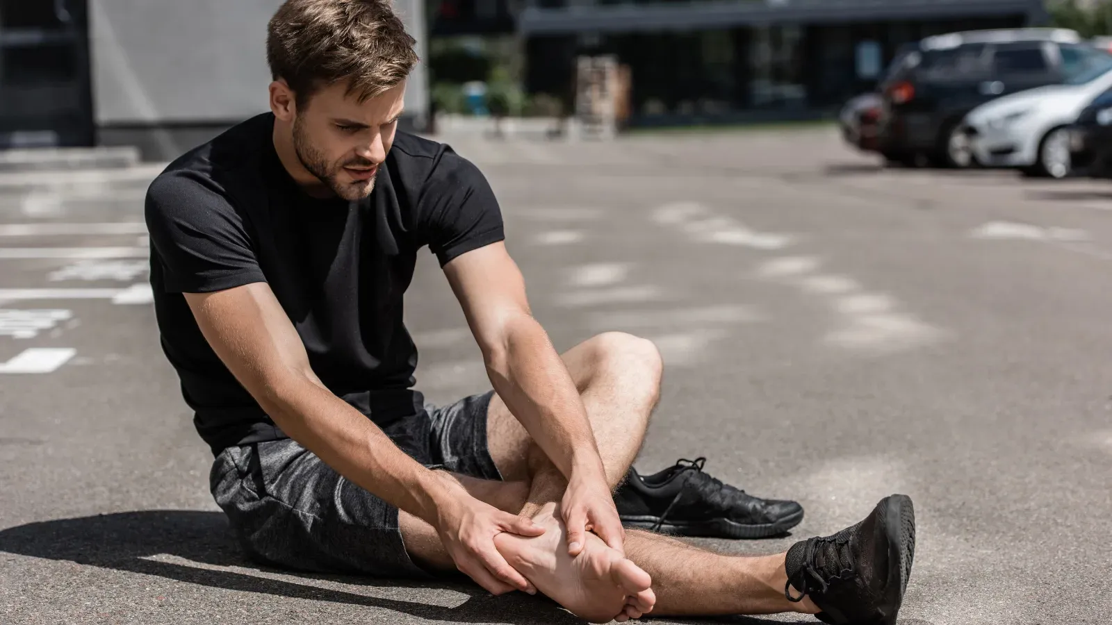 A man sitting on the road after a run, gripping the heel of one bare foot