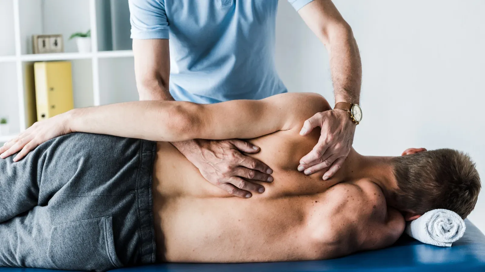A physiotherapist working with both hands across the upper back of a patient lying face down