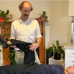 A physiotherapist lifting the straightened leg of a patient lying on a treatment table