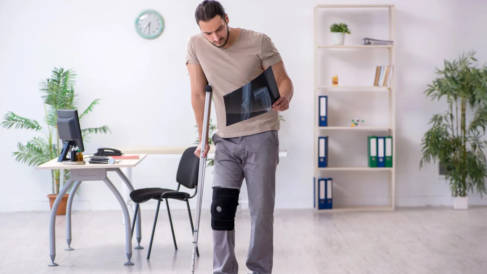 A man walking on crutches with a hinged knee brace, in an office