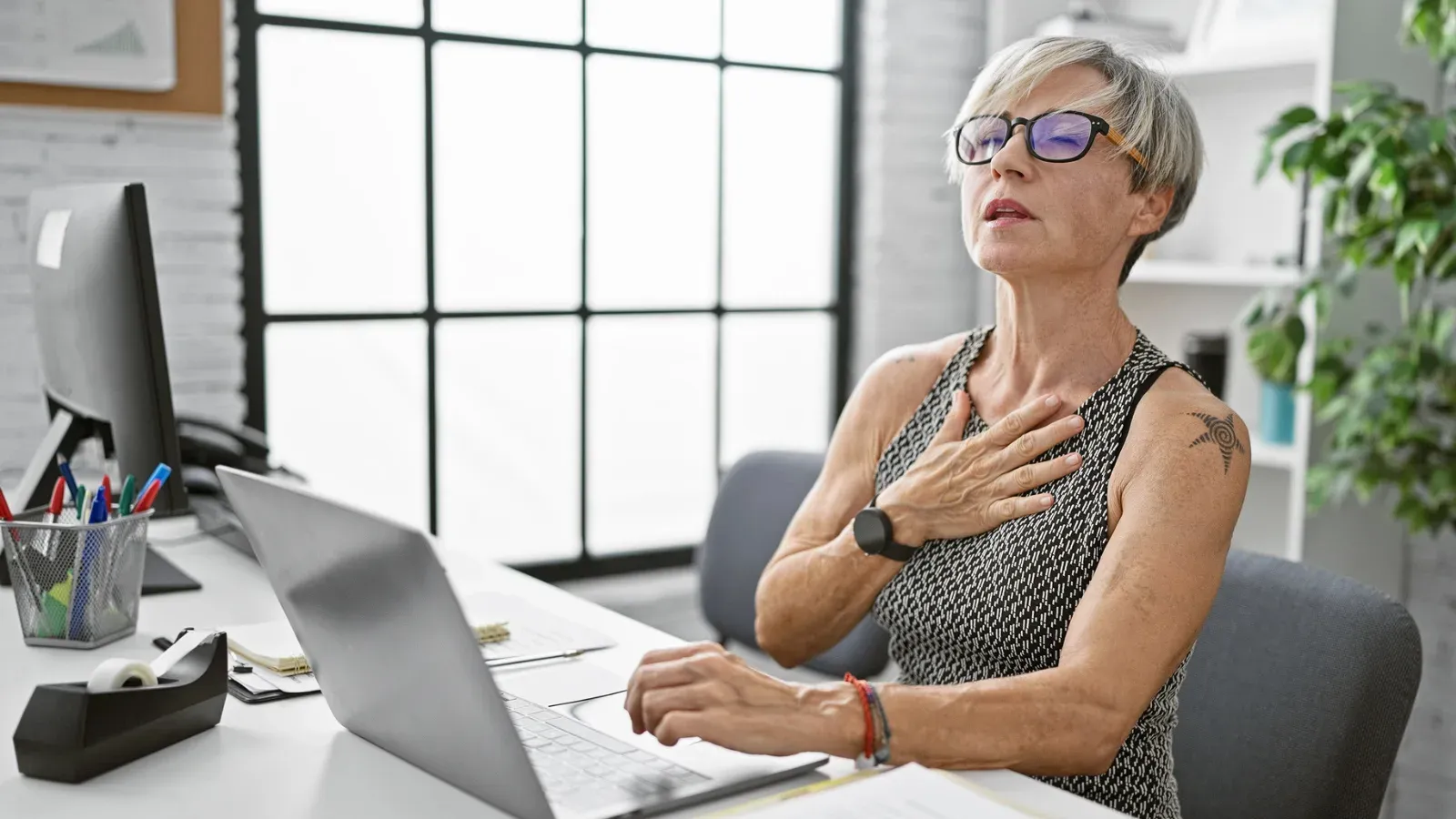 A woman at a desk pausing with a hand flat against her chest