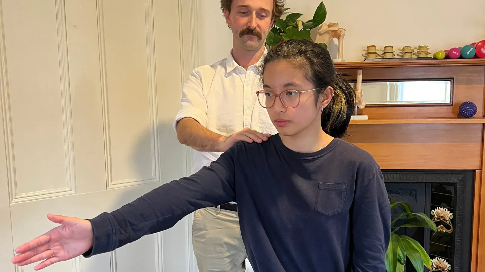 Andrew Macdonald standing behind a patient, guiding her arm out to the side to test shoulder movement