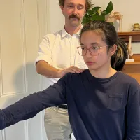 A physiotherapist standing behind a patient, steadying her shoulder as she holds her arm out to the side