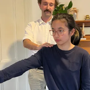 A physiotherapist standing behind a patient, steadying her shoulder as she holds her arm out to the side