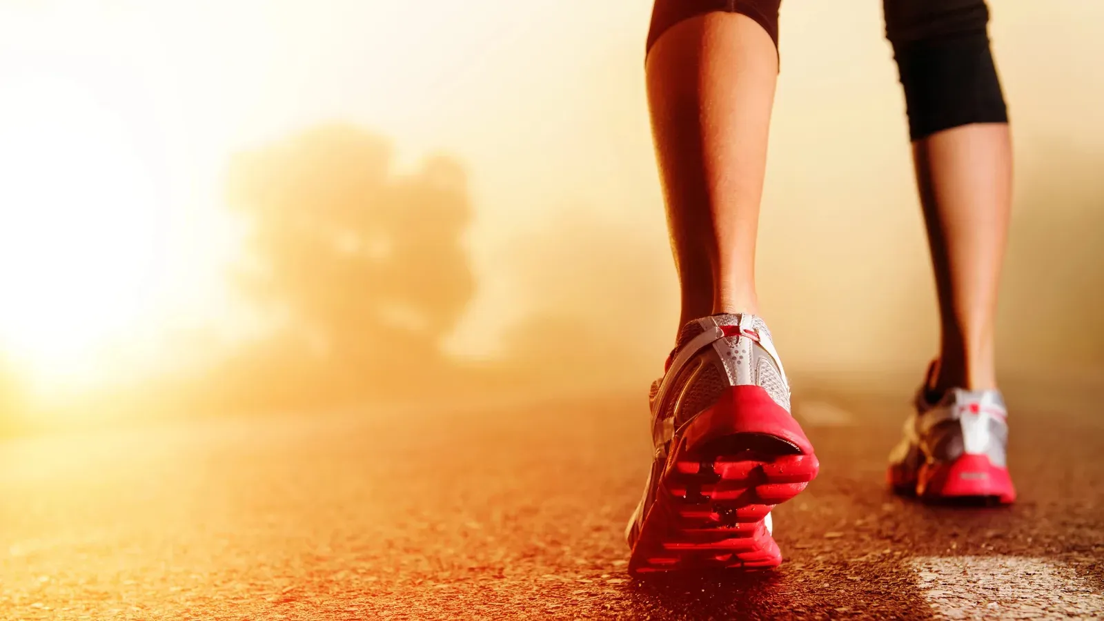 A close view of a runner's shoes striking a road at sunrise