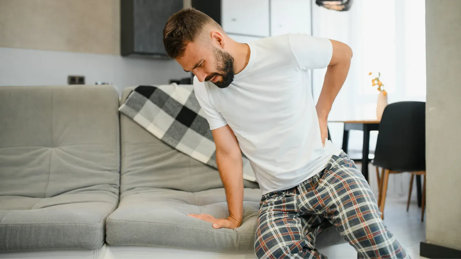A man kneeling on a sofa, one hand braced and the other pressed to his lower back