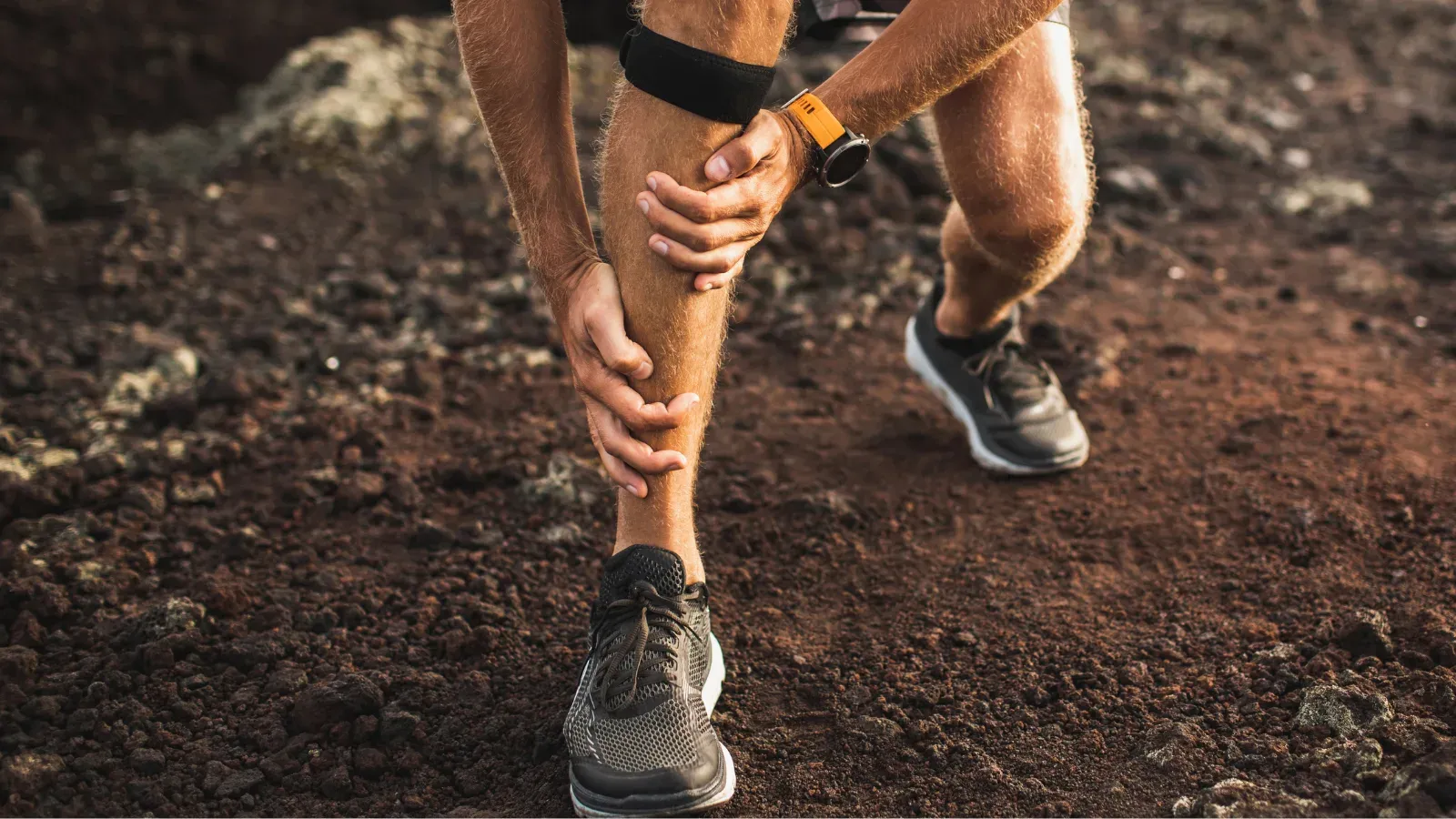 A trail runner bending to grip the front of their lower leg
