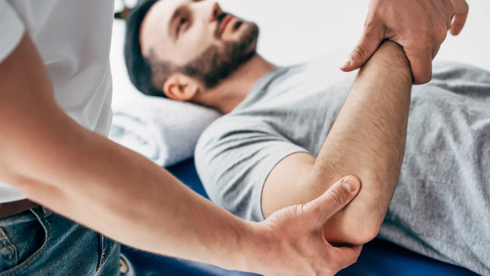 A physiotherapist supporting a patient's forearm and elbow while they lie on a treatment table