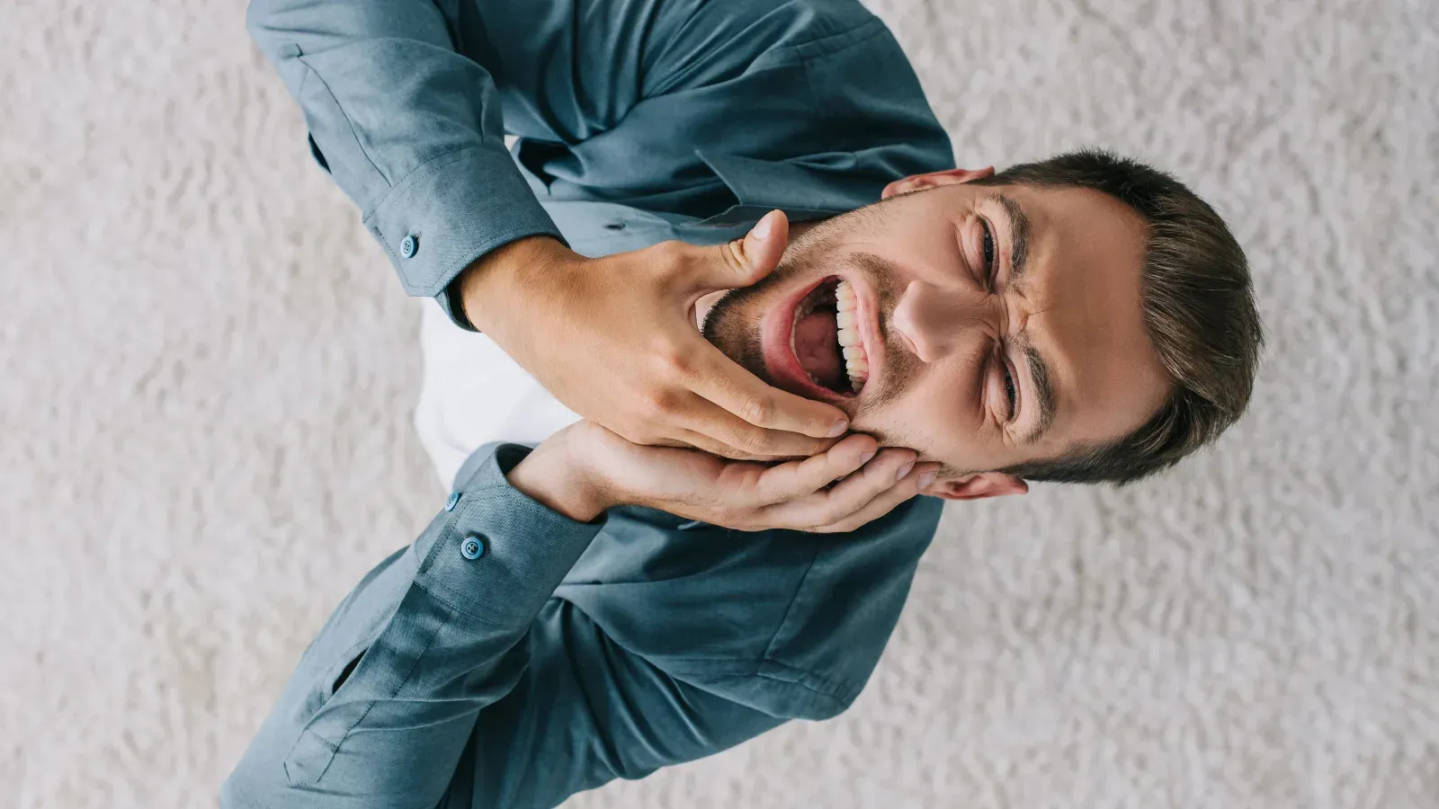 A man lying on his side with both hands to his jaw, wincing