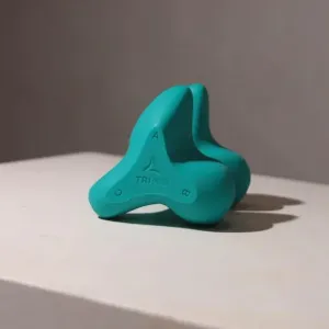 A teal three-lobed silicone device resting on a grey surface